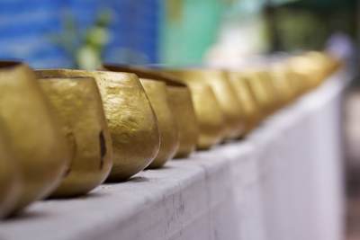 A line of gold coloured metal monks' alms bowls waiting to be filled with donations of food and money at the Phra Pathom Chedi temple in Nakhon Pathom in Thailand