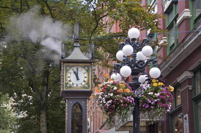 Steam clock built in 1977 sited in Water Street with flowering baskets, street sign and trees in leaf, Gastown, Vancouver, British Columbia, Canada North America