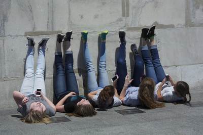Girls young women lie on their backs whilst texting using mobile telephone phones leaning against the Washington Memorial in Washington D.C. in the United States of America USA U.S.A.