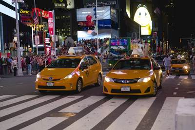 Yellow cabs taxis wait at the lights with bright neon and LED lights in Times Square at night on Manhattan Island in New York City in the United States of America USA U.S.A