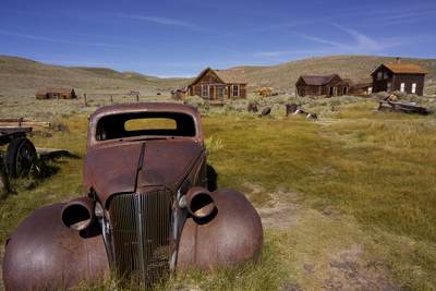 The rusting remains of a car abandoned in the 1930's with miners' houses beyond, in Bodie - a deserted gold mining town started in 1859 and after many boom and bust times, finally deserted in 1943 in California in the United States of America in the USA U.S.A.