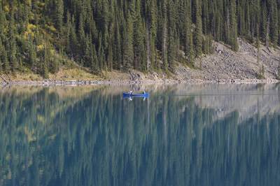 A man and woman in a blue kayak on Moraine Lake with pine and fir trees on the shore reflected in the deep blue water of the lake in Banff National Park in Alberta in Canada in North America