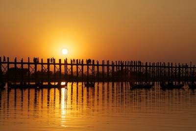 The sun sets behind the U Bein bridge - the longest teak bridge in the world, crossing Taungthaman Lake near the town of Amarapura in Myanmar (Burma)