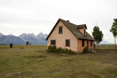 A pink stucco frame house built by John Moulton in the 1920's in the Grovont area in the Grand Teton National Park in an area known as Mormon Row, with the Grand Teton mountains in the distance in Grand Teton National Park in Wyoming in the United States of America USA U.S.A.