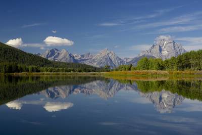 The Grand Tetons and Mount Moran viewed from the Oxbow Bend Turnout of Snake River on the Teton Park Road, with still water creating mirror reflections of the early autumn colours in Grand Teton National Park in Wyoming in the United States of America USA U.S.A.