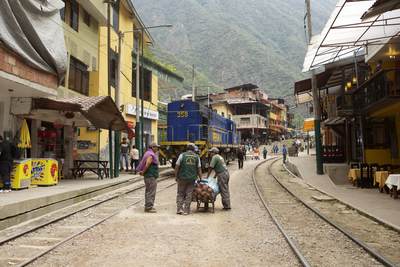 Porters wait in between the railway lines as a PeruRail train travels along the railway tracks which end in Machu Picchu Pueblo, with the track passing through the centre of the town with no barriers to prevent people straying onto the line inPeru in South America
