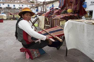 A Peruvian Woman in traditional costume weaves fabric in San Blas Square in Cusco in Peru in South America