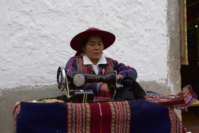 A Peruvian Woman in traditional costume sews clothes fabric using a Singer sewing machine, in San Blas Square in Cusco in Peru in South America