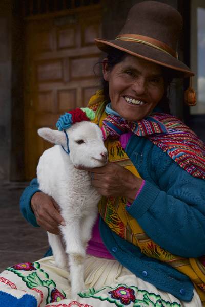 A Peruvian woman in traditional dress holds a lamb in a crocheted bonnet, in Plaza de Armas in Cusco Cuzco in Peru in South America