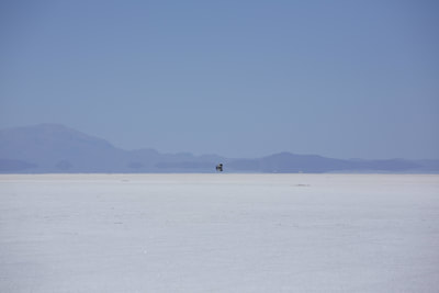A distant vehicle creates an optical illusion of distance as it crosses the bright white surface of the Salar de Uyuni - the worlds largest salt flats in Bolivia in South America