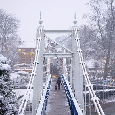Teddington Footbridge covered with snow in the winter and the Anglers pub in early evening in Teddington in Middlesex in the United Kingdom